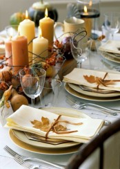 a very chic and natural Thanksgiving table setting with neutral porcelain, candles, gourds, pumpkins, berries, nuts and dried leaves