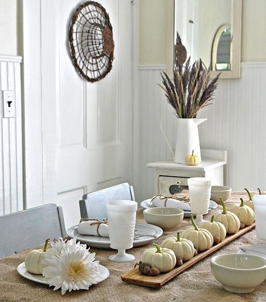 A wooden board with white pumpkins and acorns, feathers and wheat for a chic and all natural Thanksgiving table