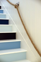 a nautical staircase with black, navy, blue and light blue steps and rope attached to the wall as railing