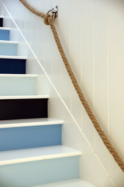 a nautical staircase with black, navy, blue and light blue steps and rope attached to the wall as railing