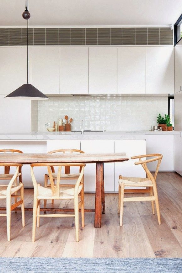 A stylish modern white kitchen with sleek cabinets, stone countertops, a rustic table and chairs, a pendant lamp