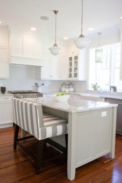 a modern neutral kitchen with white cabinets and a grey kitchen island, a white tile backsplash and white countertops, a striped loveseat and pendant lamps