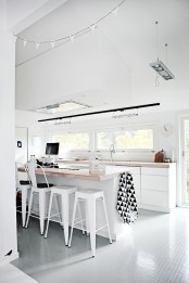 a white Scandinavian kitchen with sleek lower cabinets, butcherblock countertops, white stools and a window backsplash