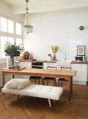 a white Scandinavian kitchen with butcherblock countertops, a white subway tile wall, a vintage wooden table and matching chairs, a statement chandelier