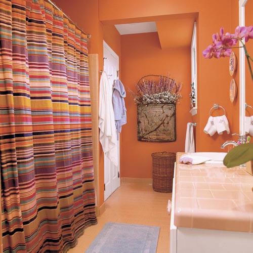 A rust colored bathroom with a warm colored floor and a bright striped curtain that includes orange touches