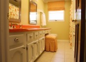 an orange countertop adds color to the neutral vanity and an orange printed shade and stool make the space more interesting