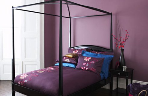 a moody bedroom with purple walls, a black cnaopy bed and blue and purple bedding is a refined and cool sleeping space
