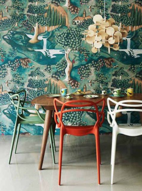 a quirky dining space done with bold flora and fauna print wallpaper, colorful chairs and a sequin chandelier