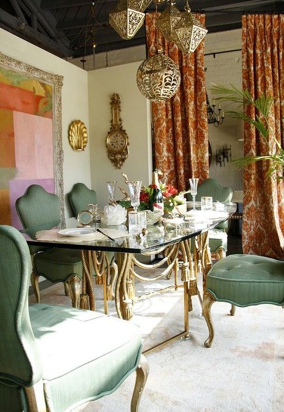 a refined Moroccan dining space with green chairs, a vintage table with tassels, a bright artwork and Moroccan lanterns