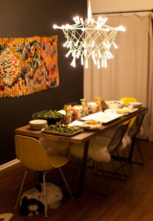 a boho dining space with a yarn artwork, a catchy modern chandelier, faux fur and a wooden table