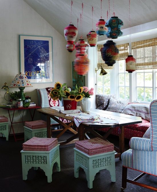 a colorful boho rustic dining room with bright yarn lamps, carved wooden furniture with upholstery and a stained wooden table