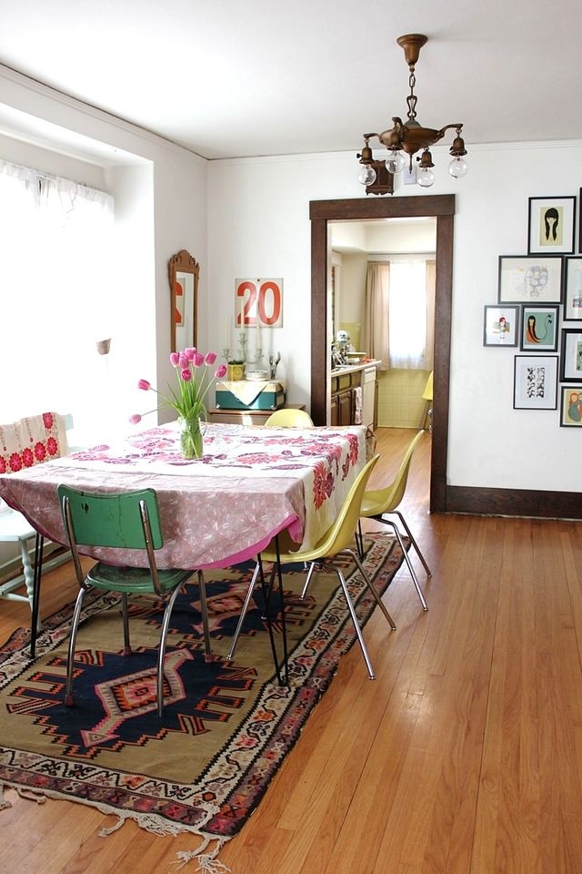 A colorful boho dining space with a hairpin leg table, mismatching chairs, a vintage chandelier and bright boho textiles
