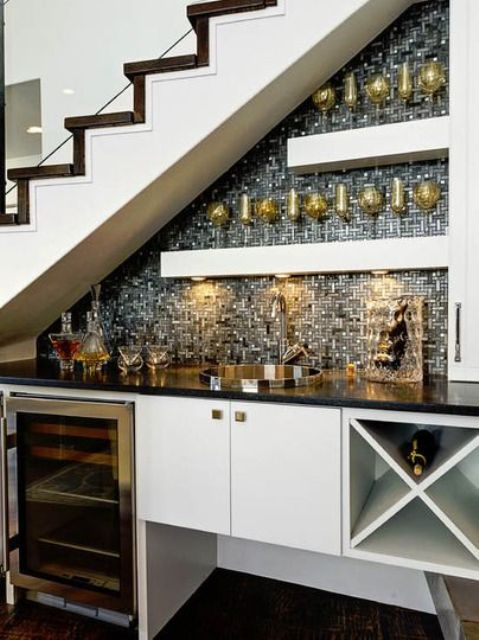 An under stairs home bar with a built in storage unit and a fridge, open shelves, shiny tiles and built in lights