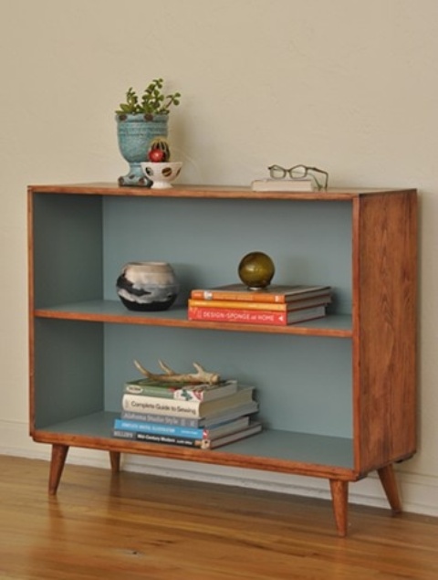 A box shaped mid century modern bookcase with muted blue lining looks chic and adds a sutble touch of color