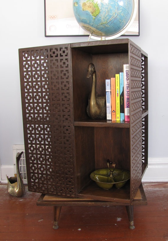 A dark colored mid century modern bookcase with laser cut doors and shelves inside