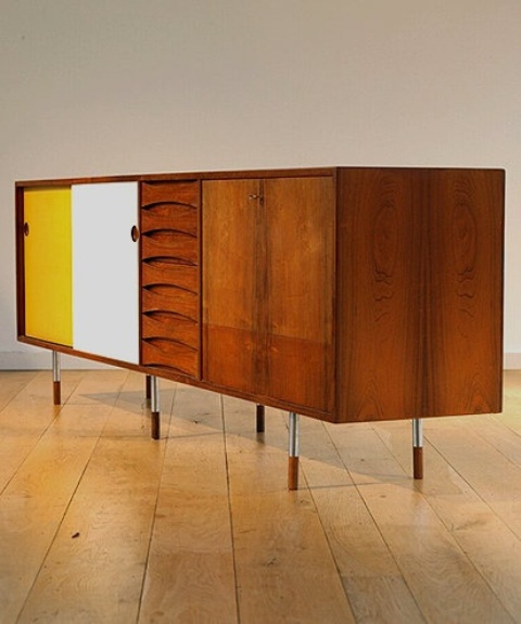 A large mid century modern sideboard with stained drawers and doors, with white and yellow doors and tall and thin metal legs is a catchy solution with a contrasting touch