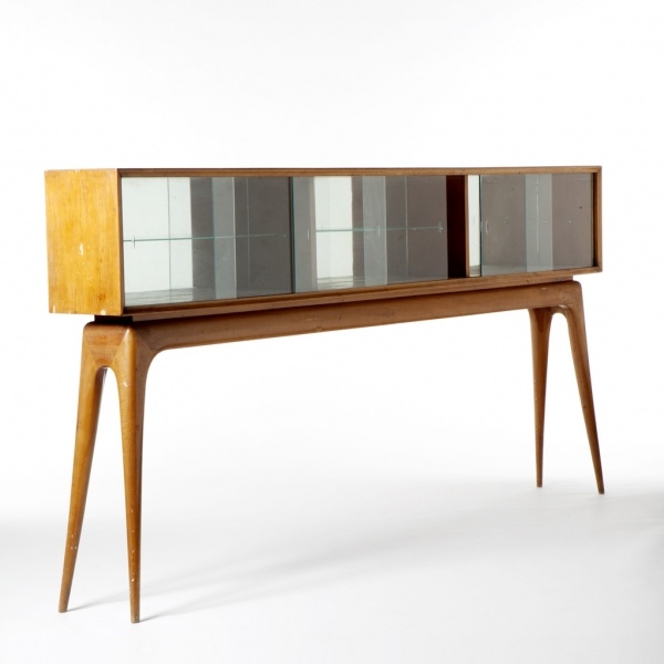 A light stained mid century modern sideboard on tall legs, with mirrror on the back and glass doors