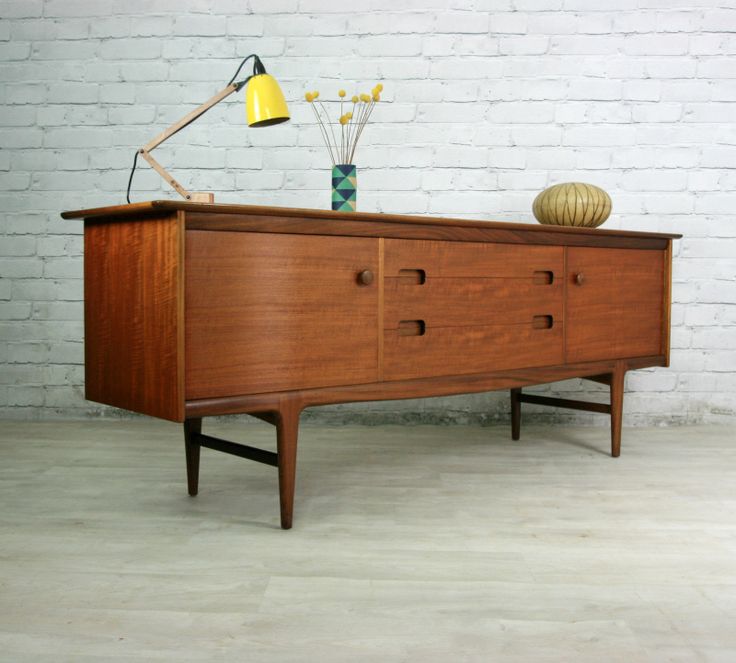 A rich stained mid century modern sideboard with doors and drawers with cutout knobws on tall legs for a mid century modern living room