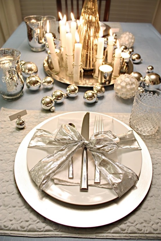 a white and metallic winter table setting with metallic ornaments, lots of candles, white and mother of pearl plates and a ribbon bow