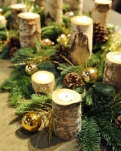 a Christmas table runner of evergreens, pinecones, metallic ornaments, tealight candles in branch candleholders