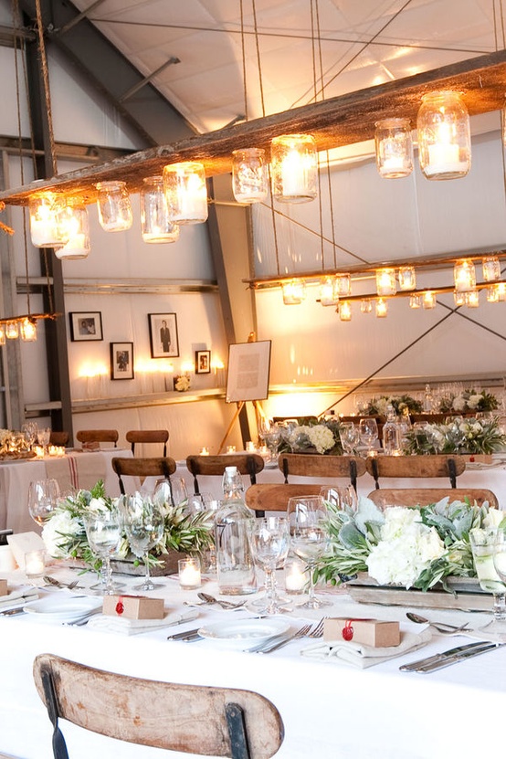 stylish and cozy winter tablescapes with pale greenery and white blooms in crates, candles and jar lights over each table