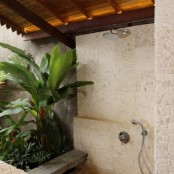 an outdoor shower all clad with stone tiles and planted tropical greenery