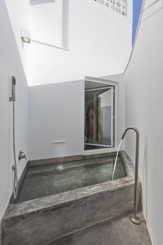 A minimalist outdoor bathroom with a built in bathtub and simple white walls