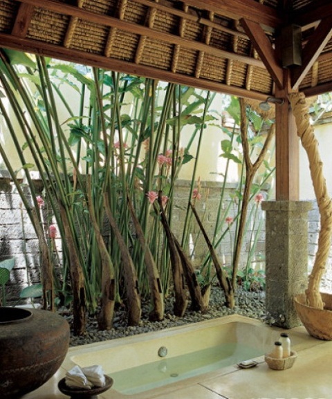 A zen like outdoor bathroom with a built in tub, pebbles, vases and living trees and greenery