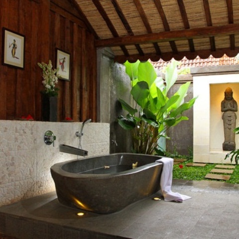 A zen inspired outdoor bathroom with lots of greenery, a stone tub and a statue