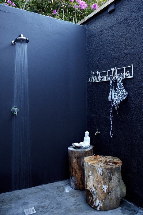 a Nordic outdoor shower done with black walls, a stone floor and a stump as a table for accessories
