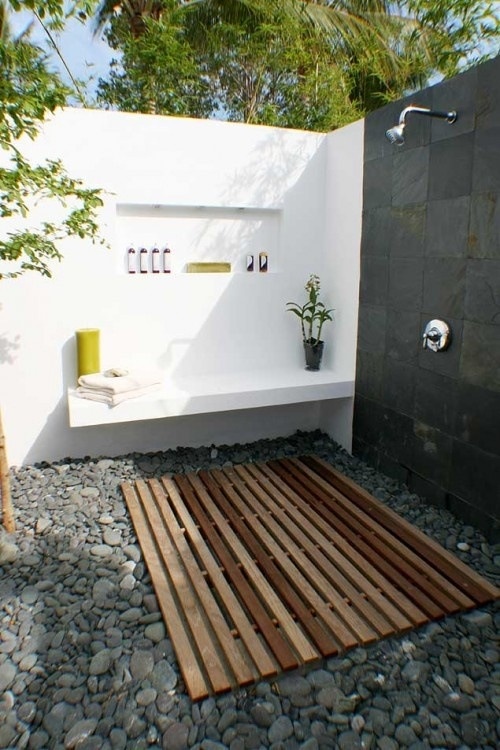 A minimalist outdoor shower with a pallet floor, pebbles, black and white walls and built in shelves