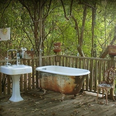 A shabby chic outdoor bathroom with a shabby bathtub and a free standing sink