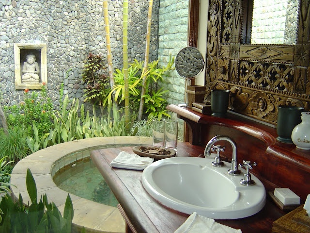 An Asian outdoor bathroom oasis with a large tub pool, a sink, an inlay mirror and much greenery