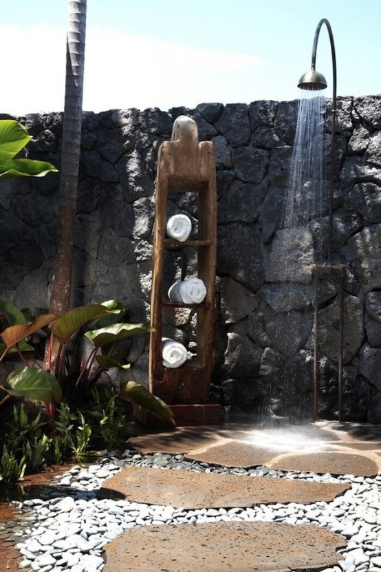 a rough outdoor shower with stone walls, pebble floors, planted greenery and a towel shelf