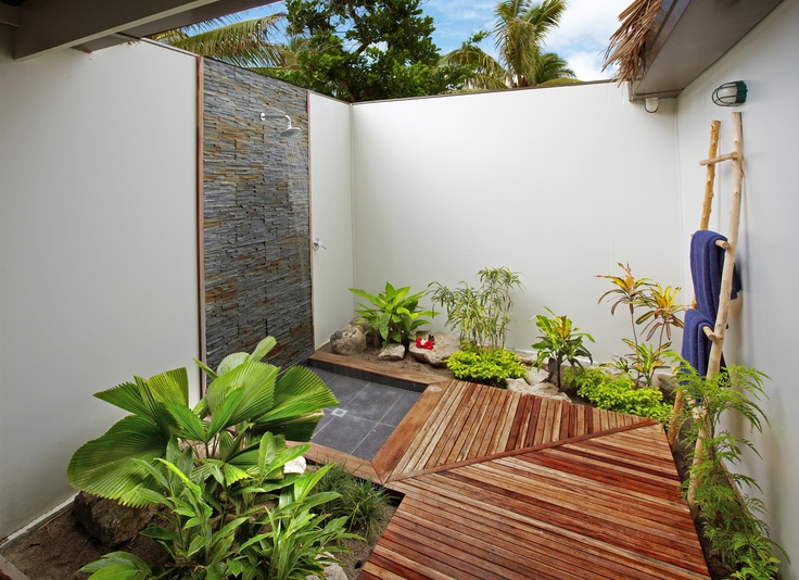 A welcoming outdoor shower nook with a wooden floor, a stone clad wall and much greenery planted here