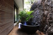 a tropical outdoor bathroom with a stone wall, a metal bathtub and potted greenery