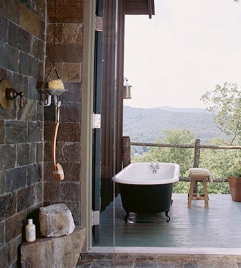 a simple outdoor bathtub with a black tub, stone side tables and a wooden bench