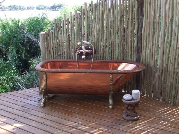A vintage inspired outdoor bathroom nook with a copper tub and a wrought side table