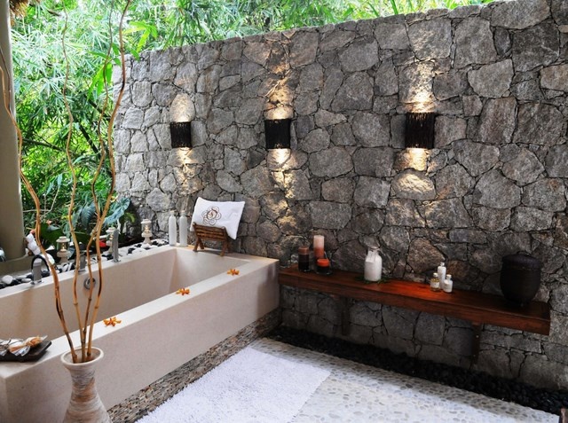 A natural space with a stone wall, a large bathtub, a shelf and built in features