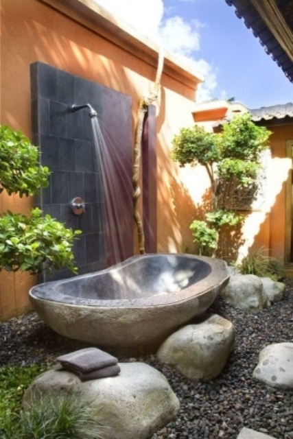 A nature inspired outdoor bathroom with stones, a metal tub, pebbles and planted greenery