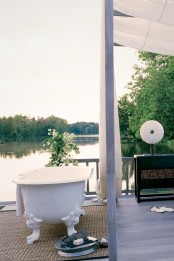 a refined outdoor bathroom with a white bathtub, potted flowers and a rug for coziness