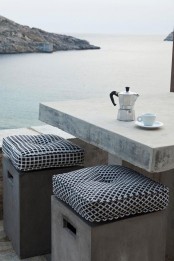 a minimalist coastal terrace with a concrete table and concrete poufs with cushions and a gorgeous sea view is a fantastic idea to rock
