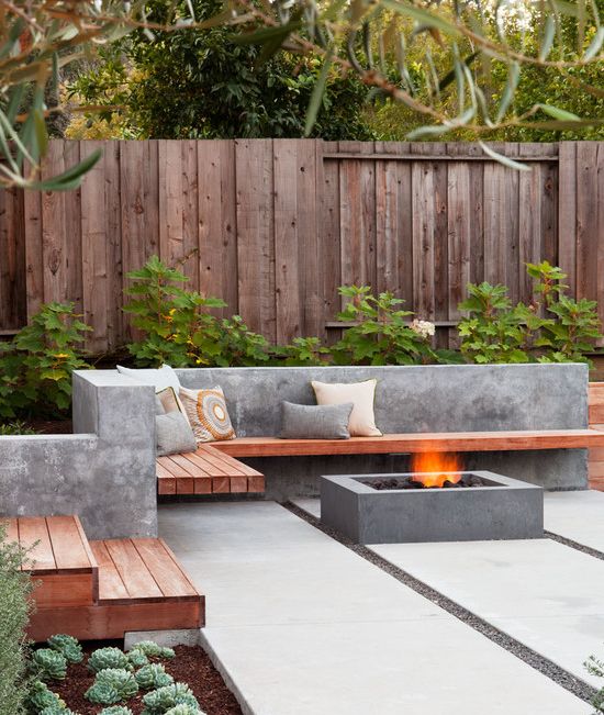 a minimalist terrace with a concrete floor, a fire pit, a concrete and wood bench and potted greenery