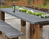 a modern rustic terrace with a reclaimed wood and concrete table and matching benches plus a planter right in the center of the table, with blooms and greenery