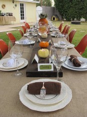a bright tablescape with a wooden table runner, pumpkin candleholders, a pumpkin vase with blooms