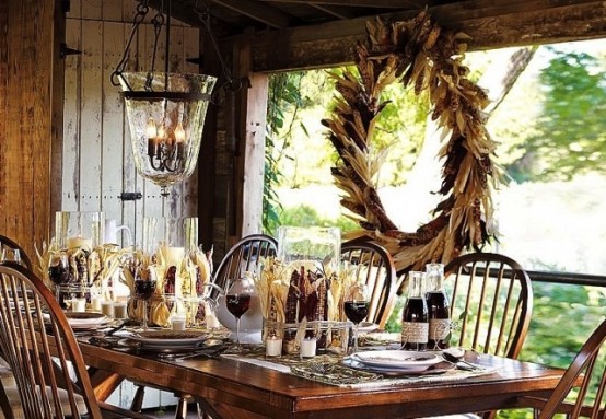 a rustic Thanksgiving tablescape with corn cobs, herbs and a matching wreath hanging next to the table and candles