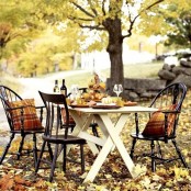 a rustic Thanksgiving table with a stand with pumpkins, fall leaves and vintage chairs with plaid pillows