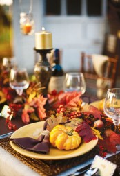 a bright Thanksgiving tablescape with bold fall leaves, pumpkins, bright napkins, berries and gold candles