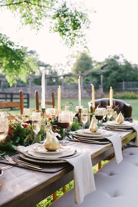 a Thanksgiving tablescape with a greenery and floral table runner, tall candles, gilded pears and printed plates