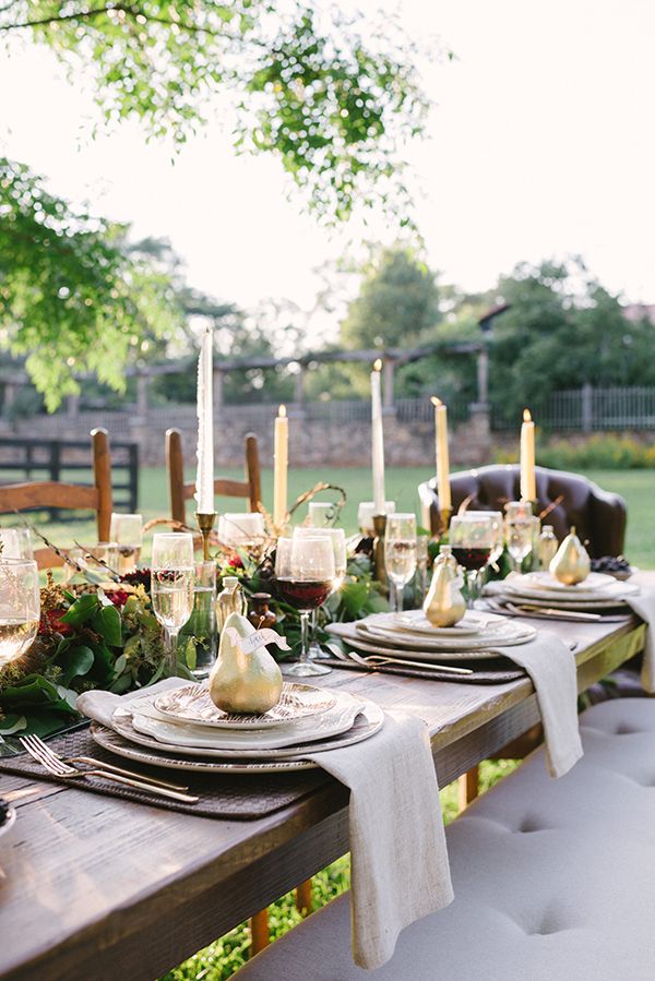 A Thanksgiving tablescape with a greenery and floral table runner, tall candles, gilded pears and printed plates